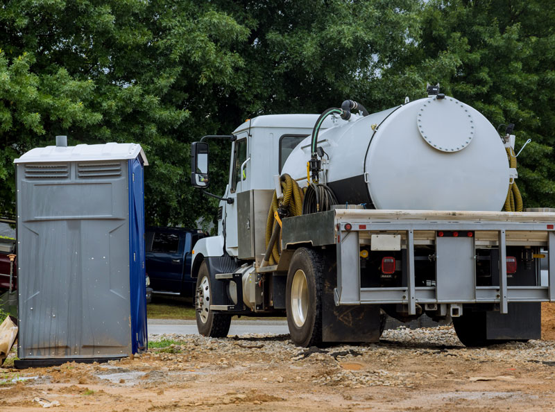 A-septic-truck-is-being-used-to-clean-portable-restrooms A septic Tank truck next to a porta potty at a construction site