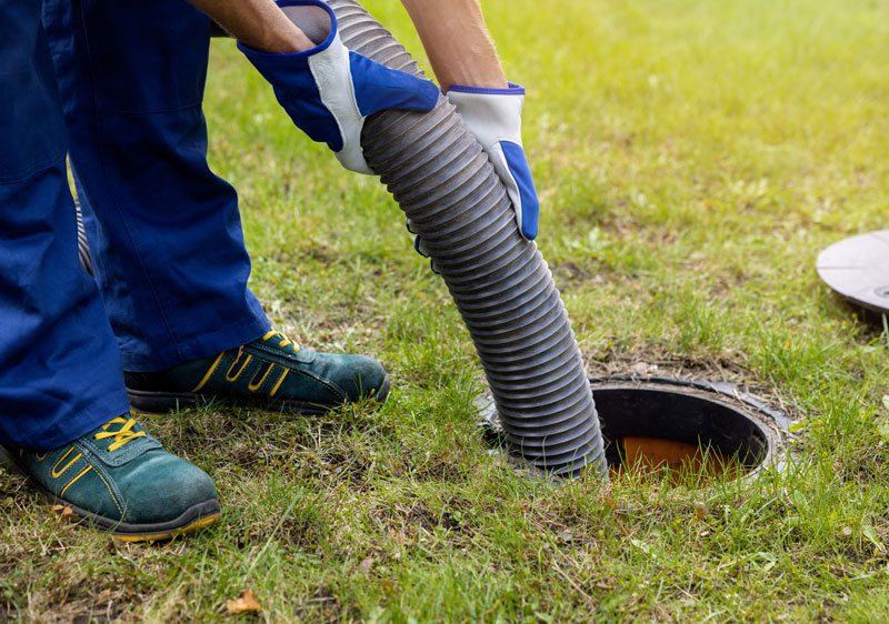 View if a man feeding hose into a septic tank.